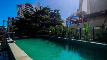 A swimming pool with a clear blue water, surrounded by greenery and modern buildings in the background.