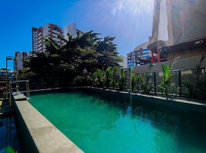 A swimming pool with a clear blue water, surrounded by greenery and modern buildings in the background. - Connect Beira Mar (Fortaleza)