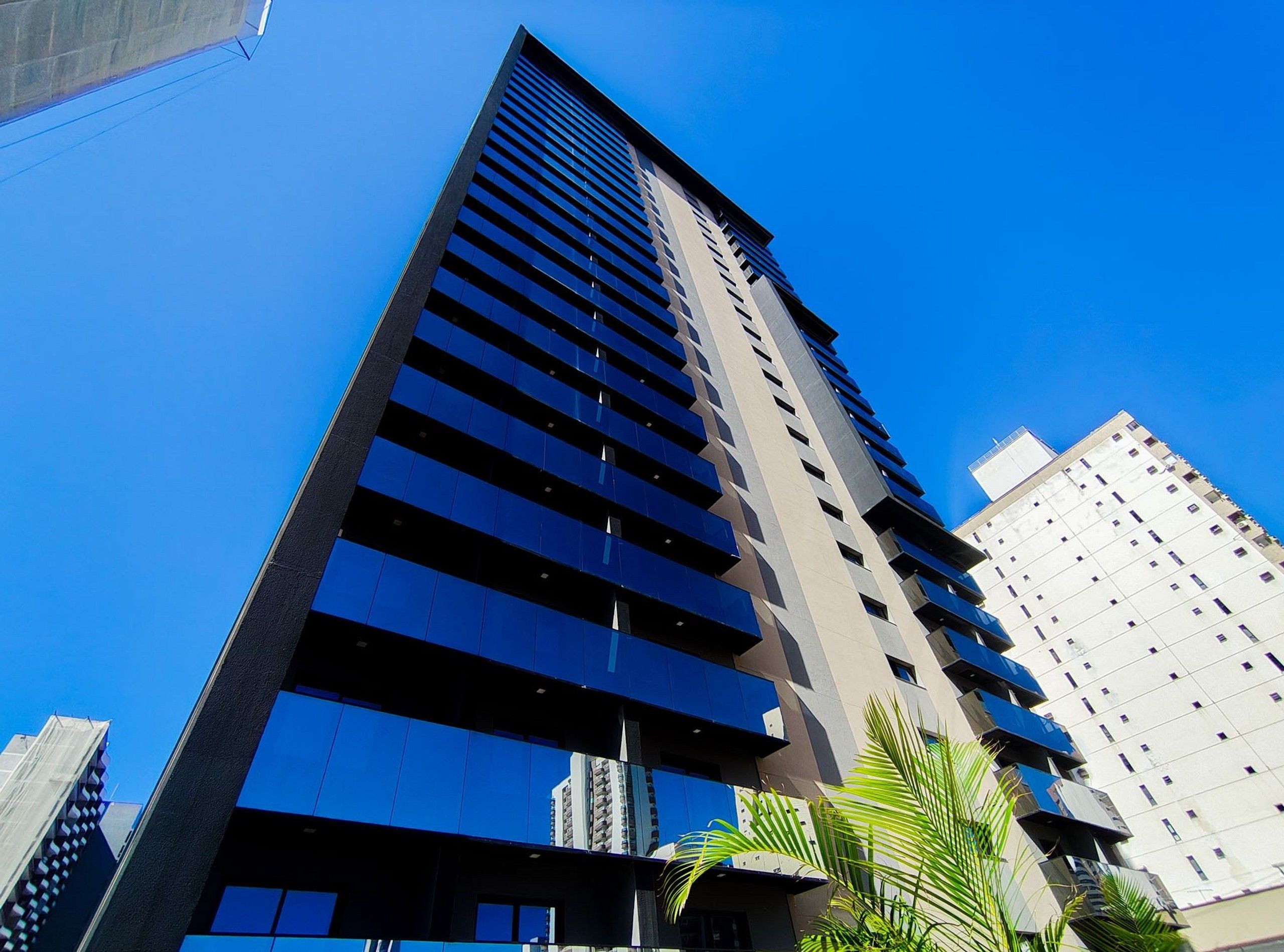 Un edificio alto y moderno con fachada de vidrio reflectante y varias balcones.