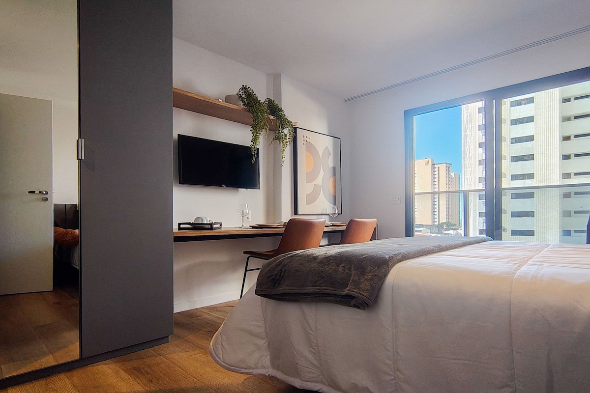 A modern hotel room with a bed, desk, and large window.