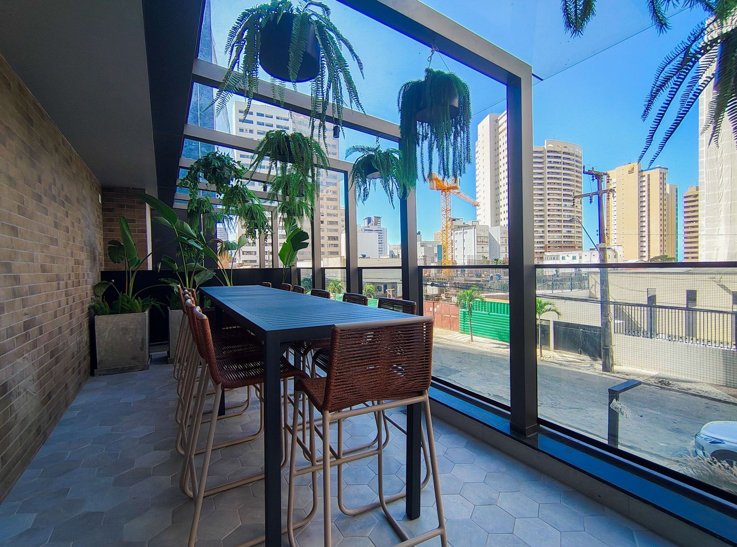 En balkon med et bord og stole, store vinduer og indeplanter.