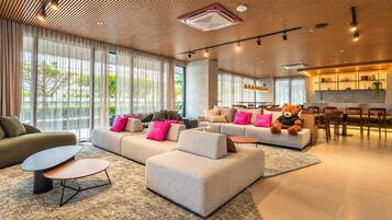 A modern hotel lobby with a seating area, a dining space, and a kitchen area.