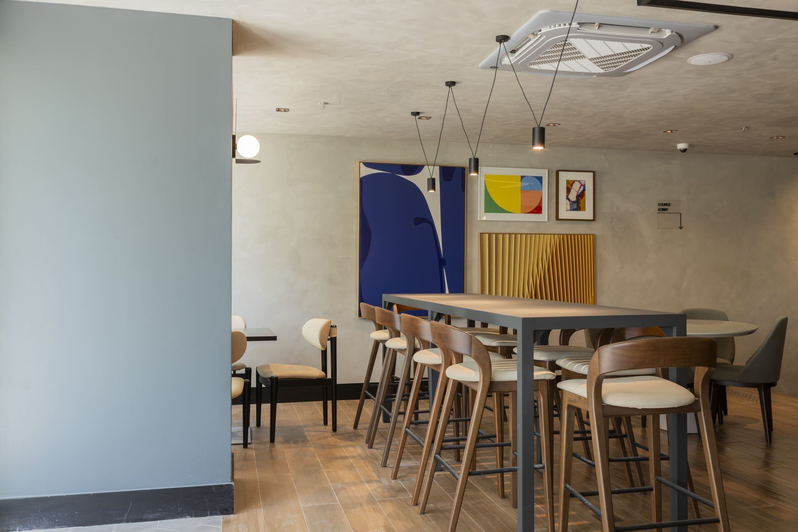 A modern dining area with a long table and multiple chairs, a blue partition, and a ceiling with recessed lighting.