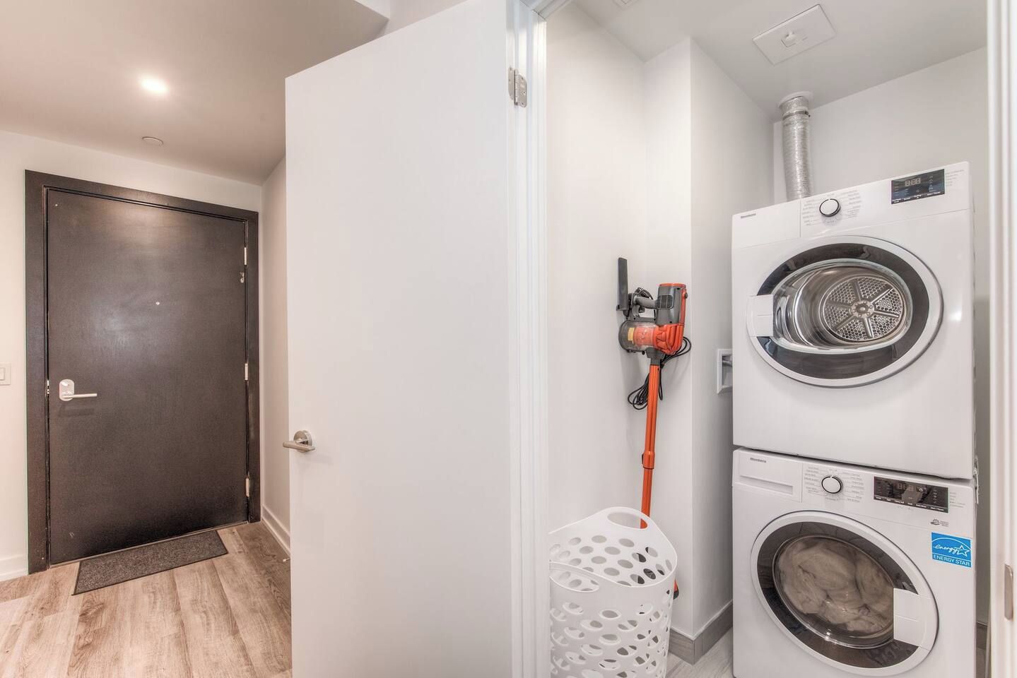 Un cuarto de lavado con lavadora y secadora, una puerta y una cesta de ropa blanca.