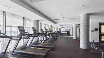 A gym with treadmills and exercise equipment, large windows, and a television screen.