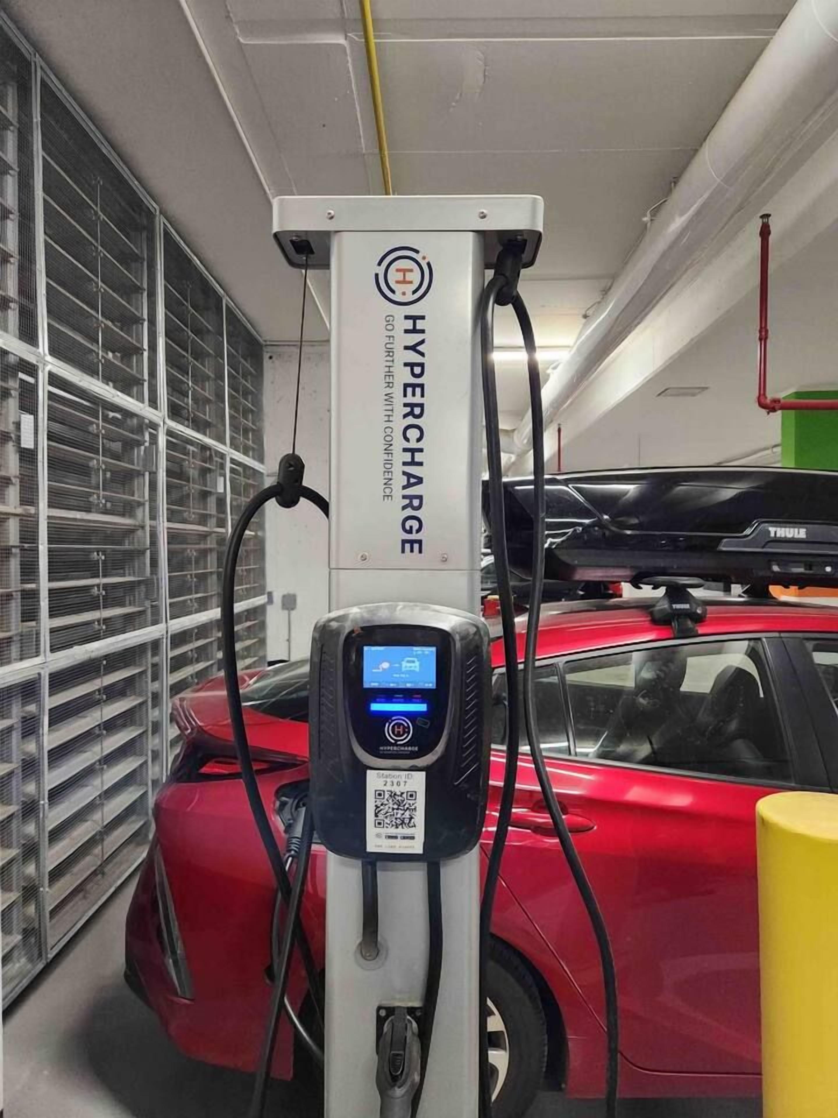 A parking garage with a charging station labeled 'Hypercharge' and a red car connected to it.