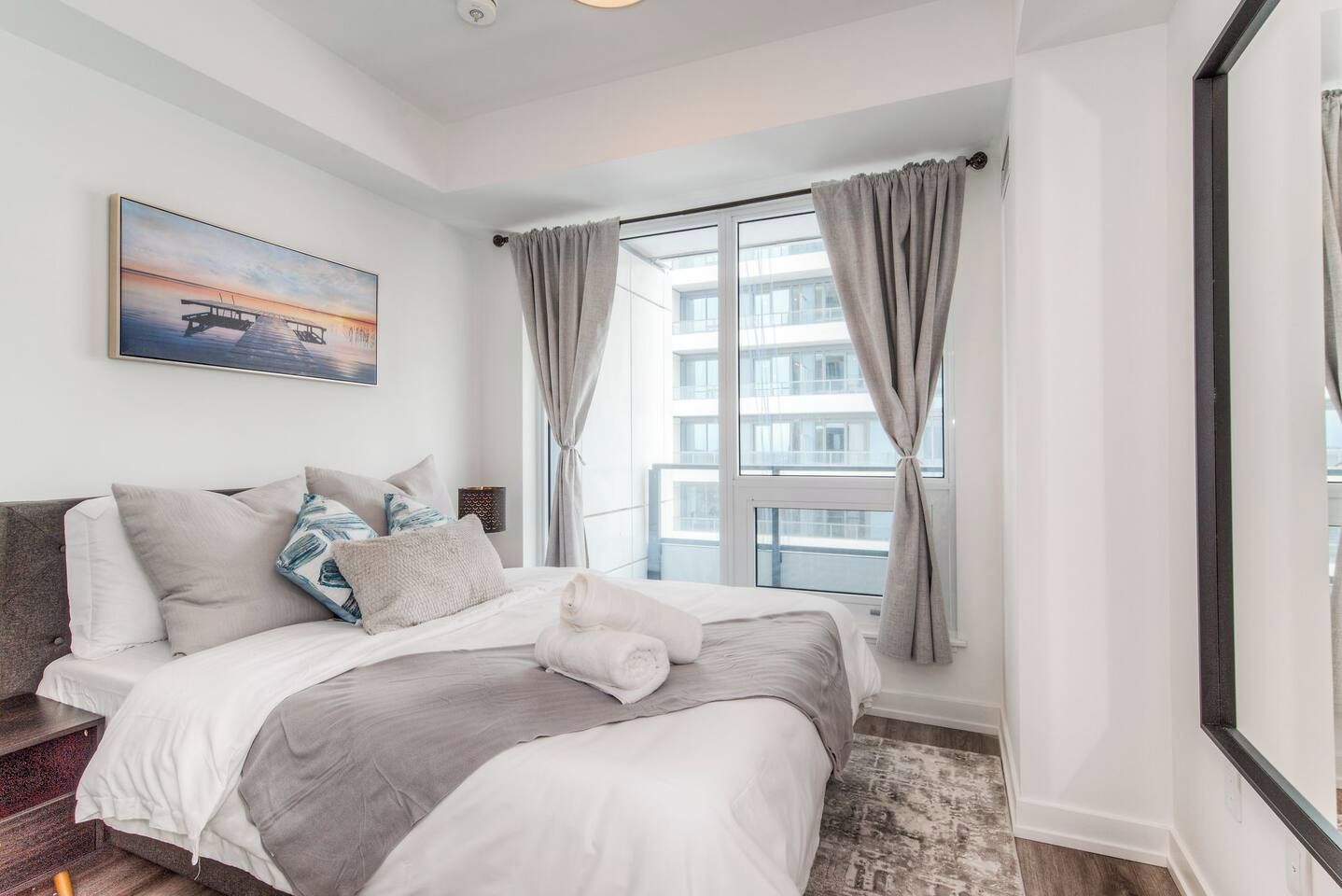 Un dormitorio moderno con una cama grande, vista a la ciudad por una ventana y un cuadro en la pared.