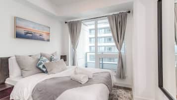 Un dormitorio moderno con una cama grande, vista a la ciudad por una ventana y un cuadro en la pared.