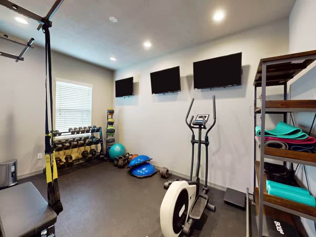 A home gym with exercise equipment, a rack of dumbbells, and a wall-mounted TV.