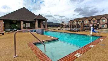 A swimming pool with a lifeguard stand, a covered seating area, and a brick building in the background.