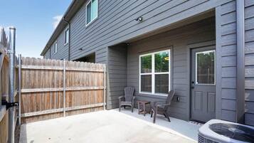 A residential exterior with a gray siding house, a wooden fence, two chairs, a table, and an air conditioning unit.