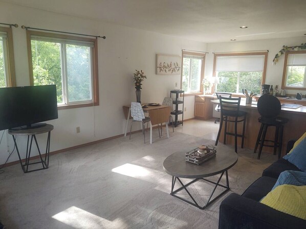 Una sala de estar con televisor, mesa de centro, sofá y un área de comedor con sillas y mesa.