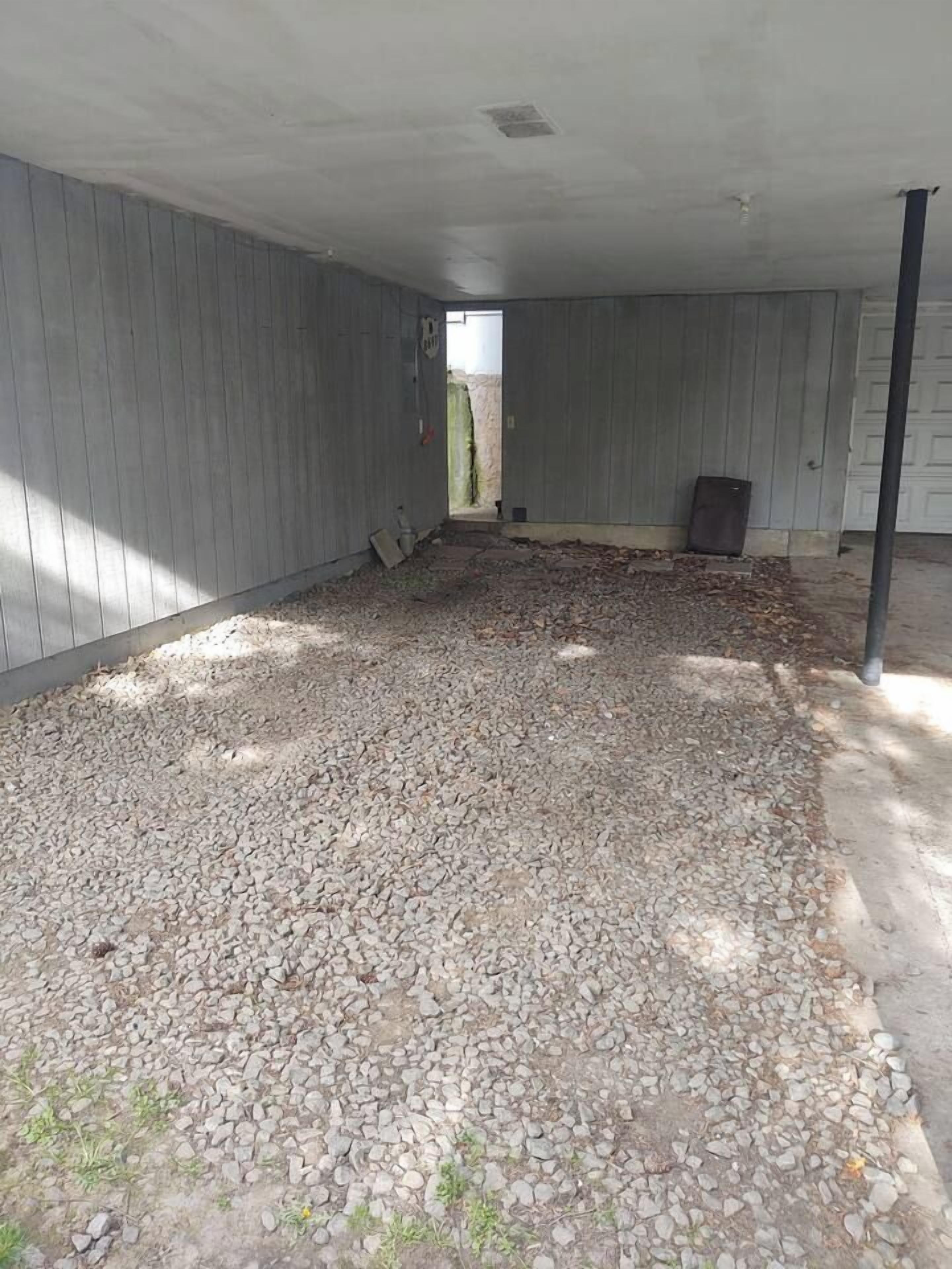 Ein Innenraum mit Kiesboden, Holzwänden und einer sichtbaren Tür zum Außenbereich.