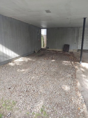 Un espacio interior con piso de grava, paredes de madera y una puerta visible que da al exterior.