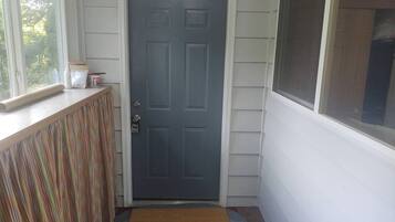 A door with a doormat, a window, and a small shelf with items.
