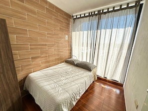 A room with a bed, wooden wall paneling, a window with curtains, and a door. - Tremendous 7-bedroom building in Heroica Puebla de Zaragoza (Heroica Puebla de Zaragoza)