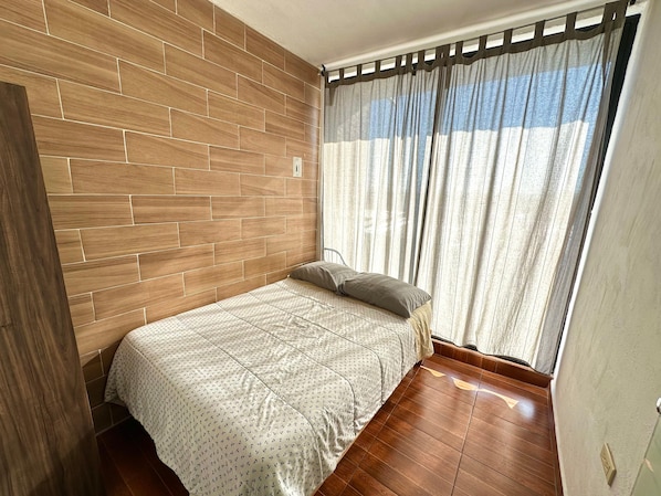 Ein Zimmer mit einem Bett, Holzvertäfelung, einem Fenster mit Vorhängen und einer Tür.