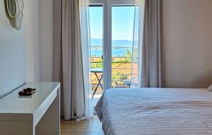 Ein Schlafzimmer mit Bett, Schreibtisch und Blick auf einen Balkon mit Gartenmöbeln.