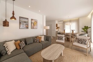 A modern living room with a grey sectional sofa, a wooden coffee table, and a dining area with a table and chairs. - Beachside Hideaway - Elegant Coastal Getaway (Peniche)