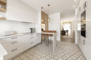 A modern kitchen with white cabinetry, a built-in oven, and a dining area with a table and chairs. - Beachside Hideaway - Elegant Coastal Getaway (Peniche)