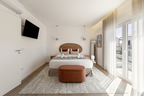 A modern bedroom with a large bed, a flat-screen TV, a wooden headboard, a side table, a mirror, and a view of the outside through large windows. - Beachside Hideaway - Elegant Coastal Getaway (Peniche)