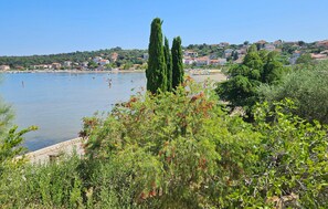 Uma vila costeira com vista clara para o mar, uma praia arenosa e vegetação densa em primeiro plano.