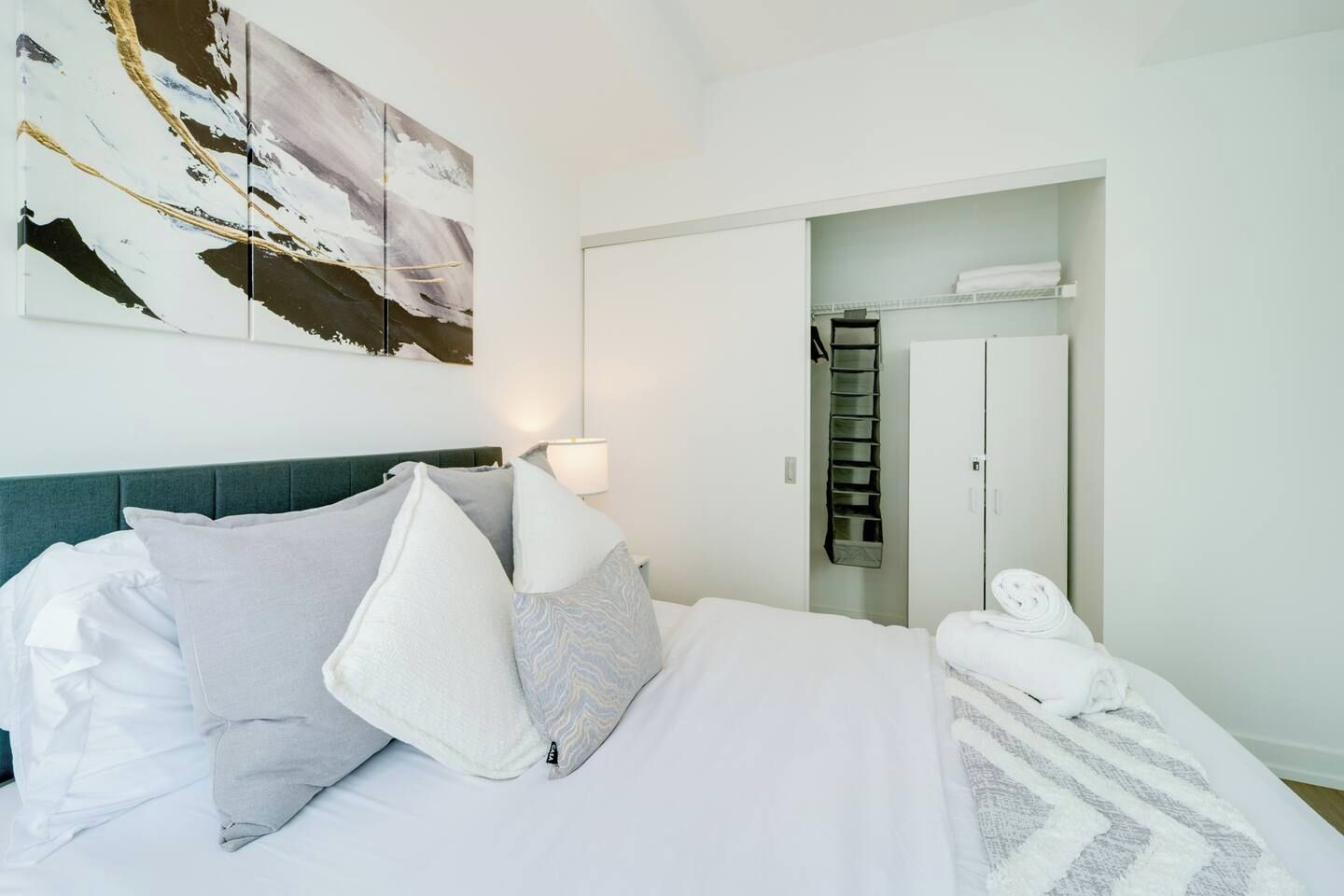 Une chambre d’hôtel avec un lit, des oreillers, une lampe de chevet, une armoire et une serviette sur le sol.