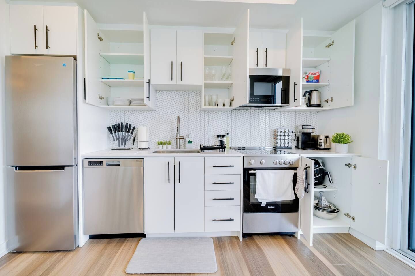 A modern kitchen with white cabinetry, stainless steel appliances, and a herringbone tile backsplash.
