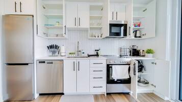 A modern kitchen with white cabinetry, stainless steel appliances, and a herringbone tile backsplash.