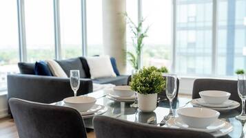 A dining area with a table set for four, including plates, bowls, cutlery, and glasses. There is a potted plant on the table, and the room has large windows with a view of the city.