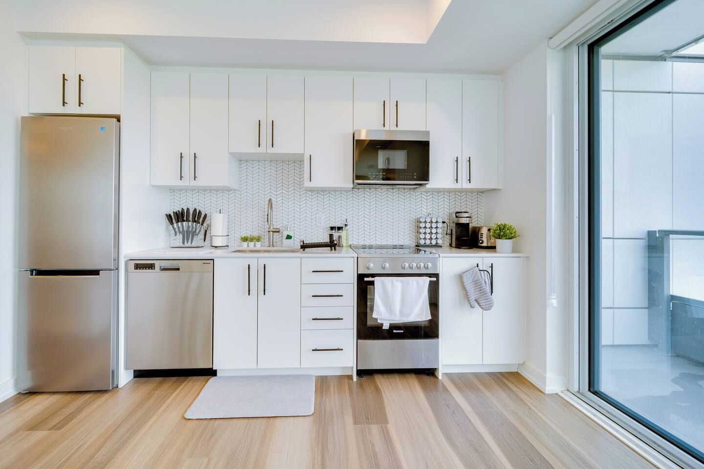 Una cocina moderna con armarios blancos, un refrigerador de acero inoxidable, un microondas, un horno y un lavavajillas.