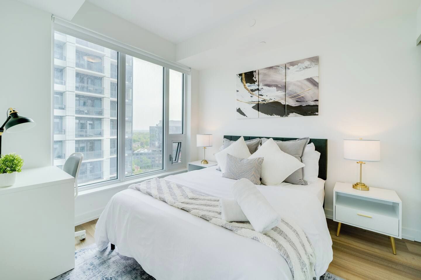 Un dormitorio moderno con una cama grande, mesitas de noche, un escritorio y un ventanal con vista a la ciudad.