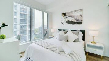 Un dormitorio moderno con una cama grande, mesitas de noche, un escritorio y un ventanal con vista a la ciudad.
