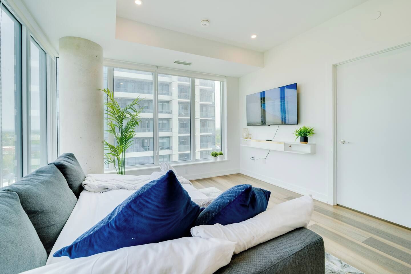 A modern living room with a sofa, a flat-screen TV, a large window, and a plant.