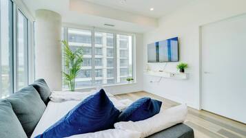 A modern living room with a sofa, a flat-screen TV, a large window, and a plant.