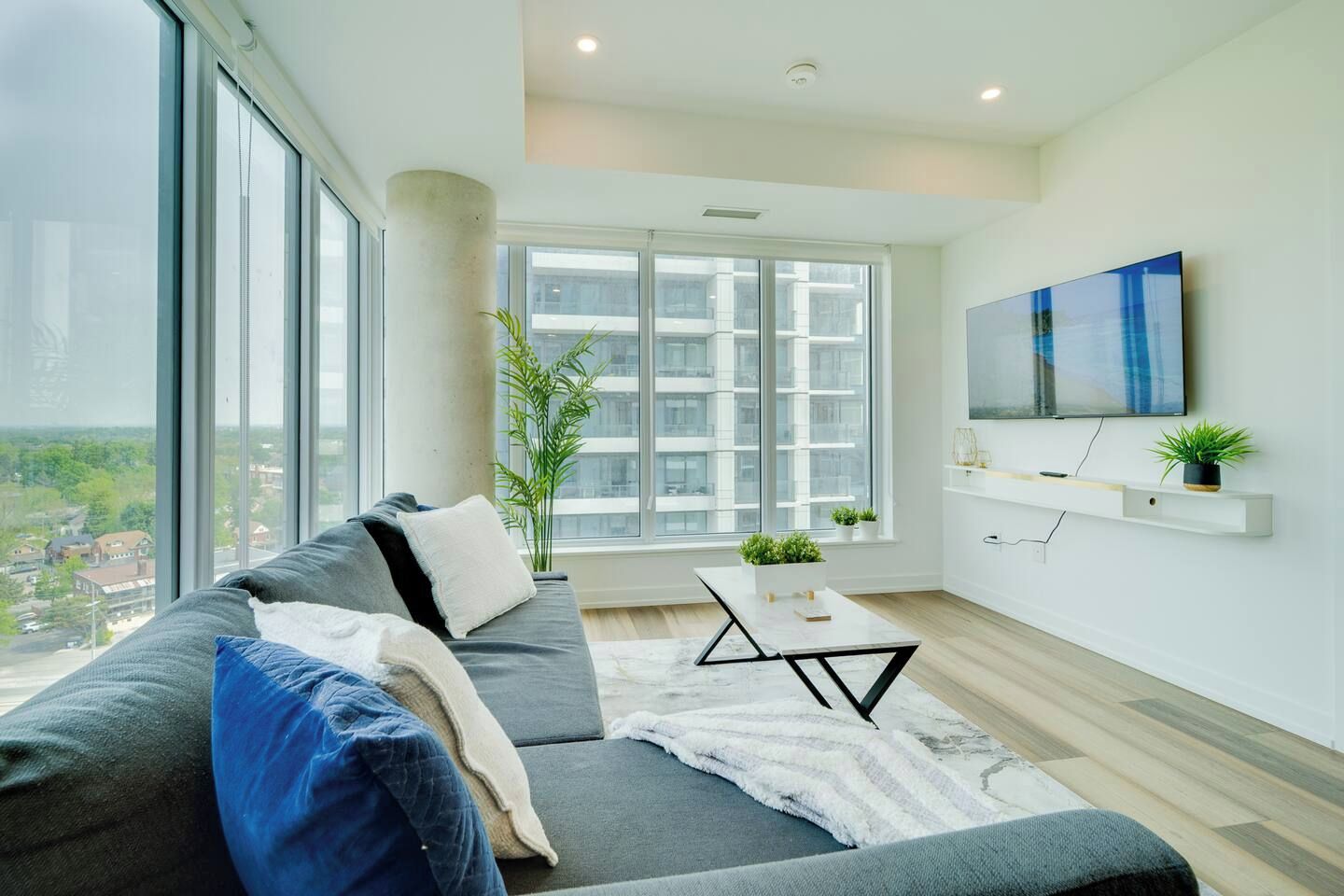 Una sala de estar moderna con sofá, una mesa de centro y un amplio ventanal con vista a la ciudad.