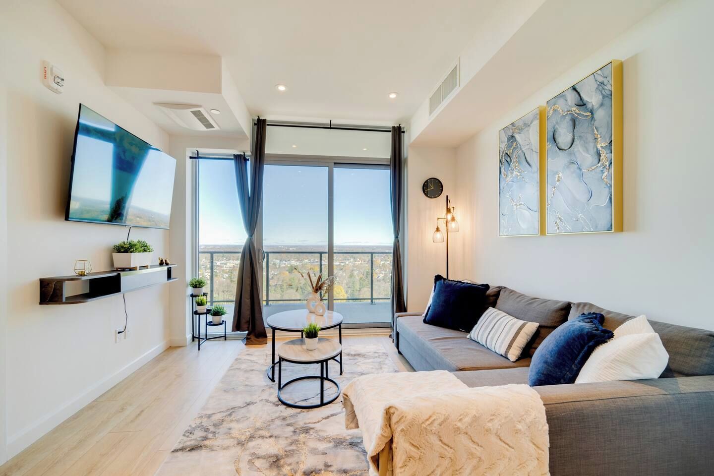 Una sala de estar moderna con un sofá, un televisor de pantalla plana, una mesa redonda con plantas y un ventanal con vistas.