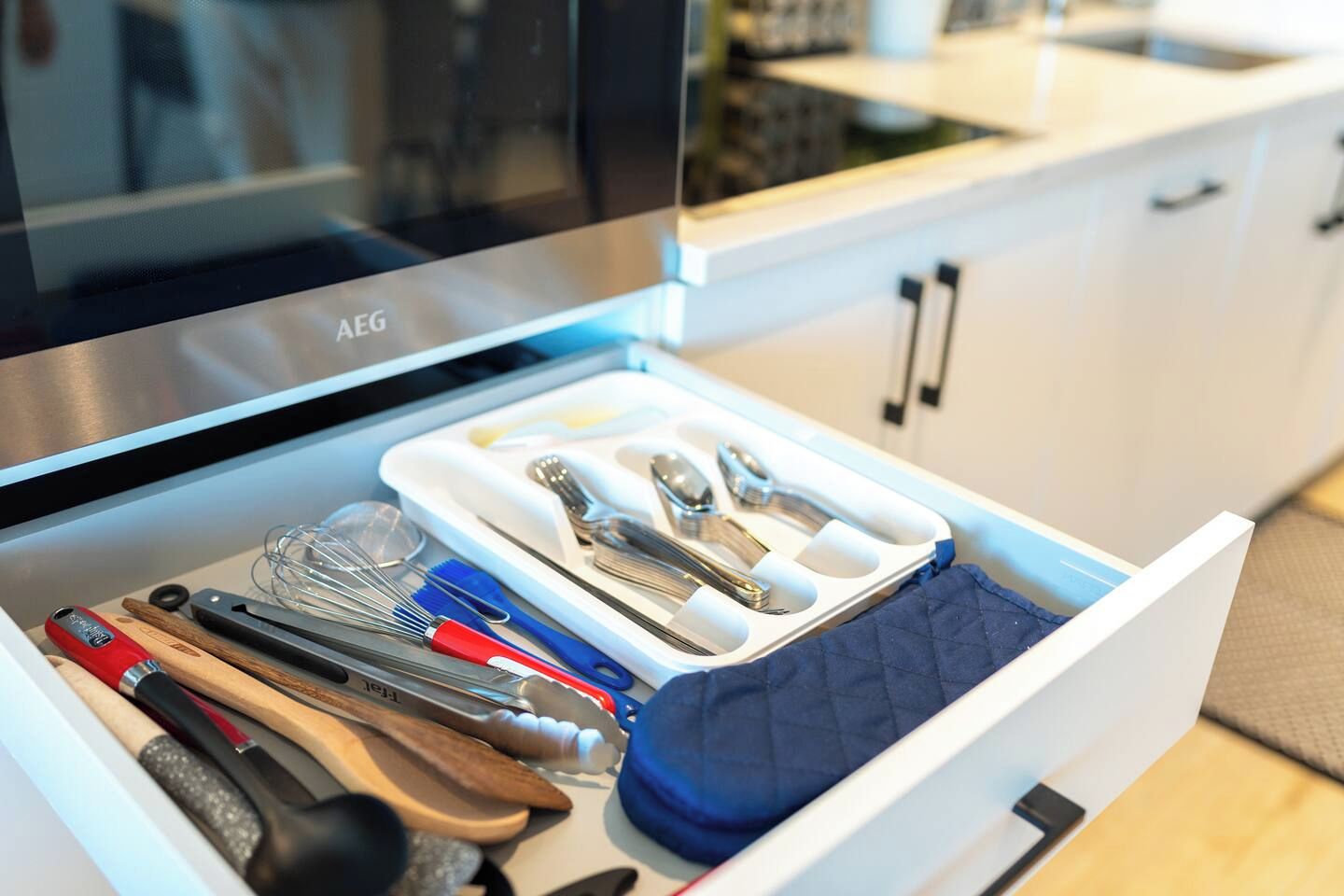 A kitchen drawer with utensils and a blue cloth.