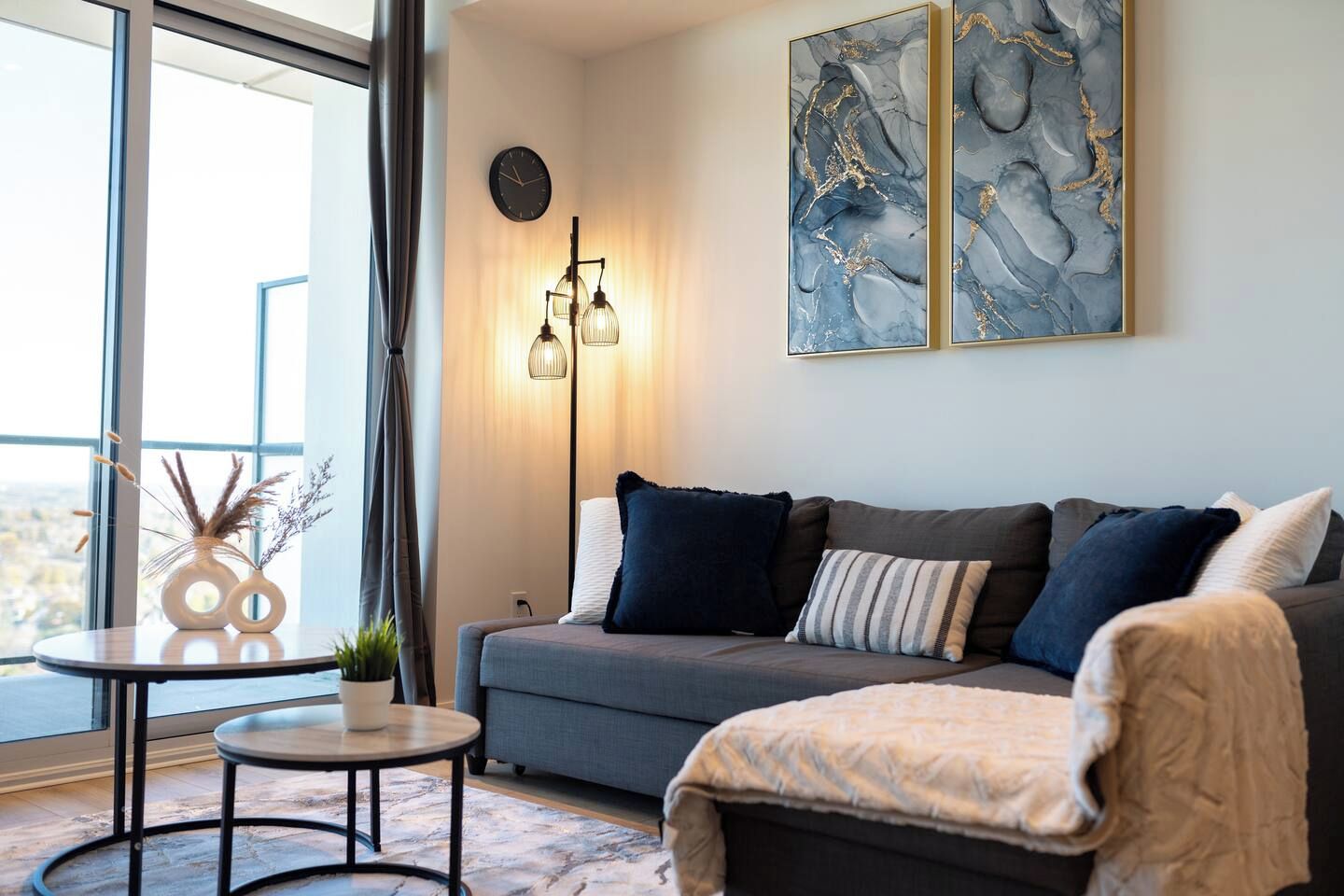 Un salon moderne avec un canapé gris, une petite table ronde et un lampadaire.