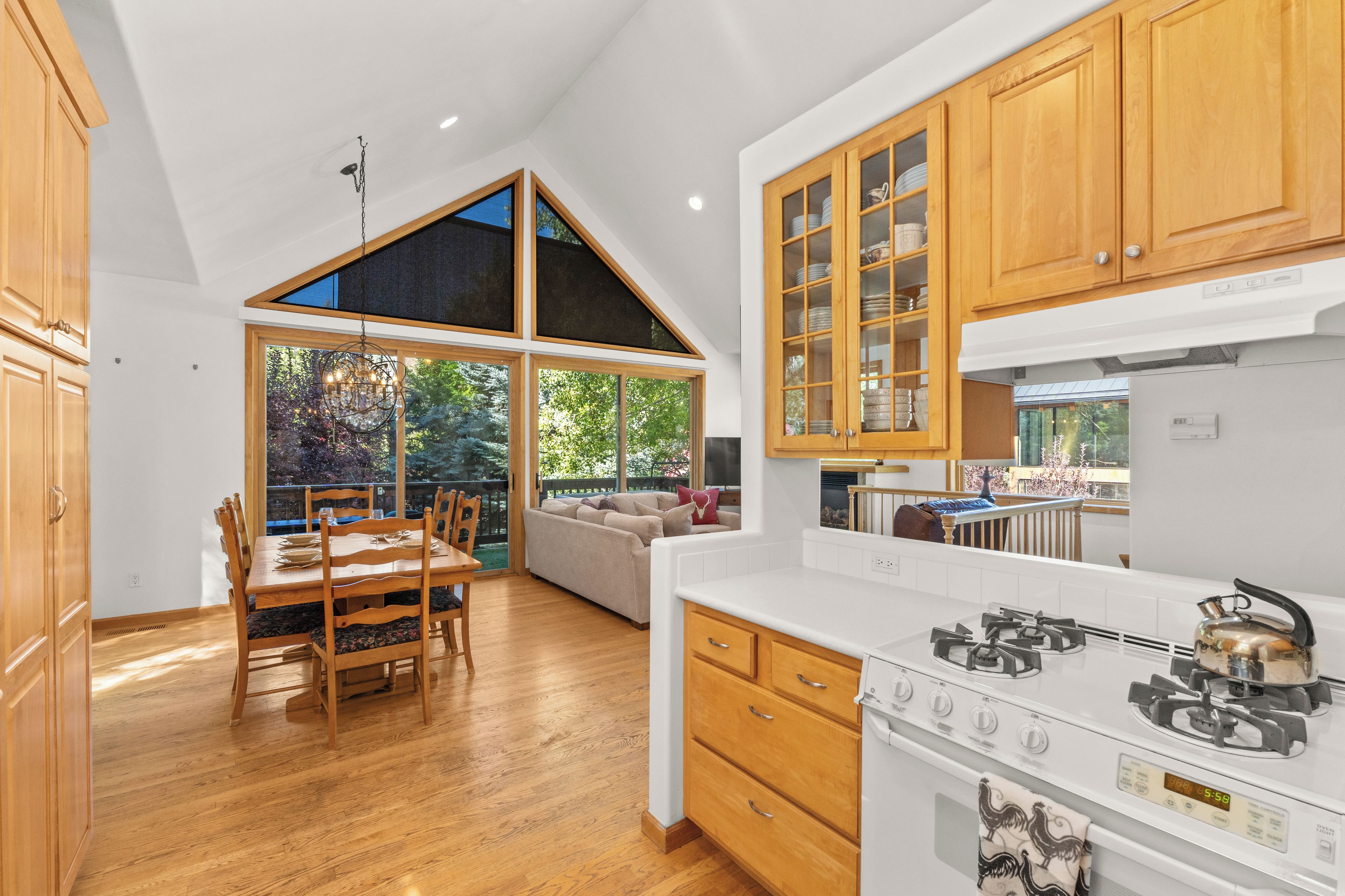 A modern kitchen with wooden cabinets, a dining area with a table and chairs, and a large window offering a view of the outdoors.