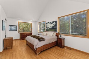 Un dormitorio con una cama grande, suelo de madera y ventanas amplias con persianas.