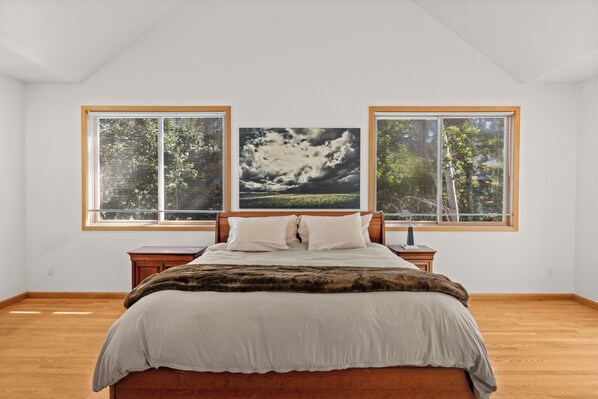 Une chambre à coucher avec un lit, une table de chevet, une lampe et une grande fenêtre avec des stores.