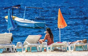 A beach with lounge chairs, a blue and an orange umbrella, and a small boat in the water. - Amazing home in Slatine (Slatine)