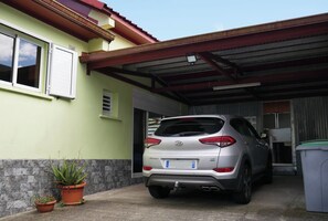 Een zilveren auto geparkeerd in een overdekte garage, met een huis op de achtergrond.