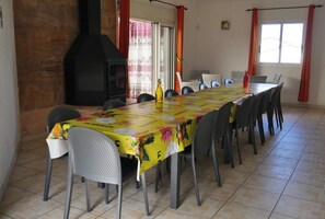 A dining area with a long table, chairs, a central pillar, and a fireplace. - L'IDOLIVIER, location de vacances (La Plaine-des-Palmistes)
