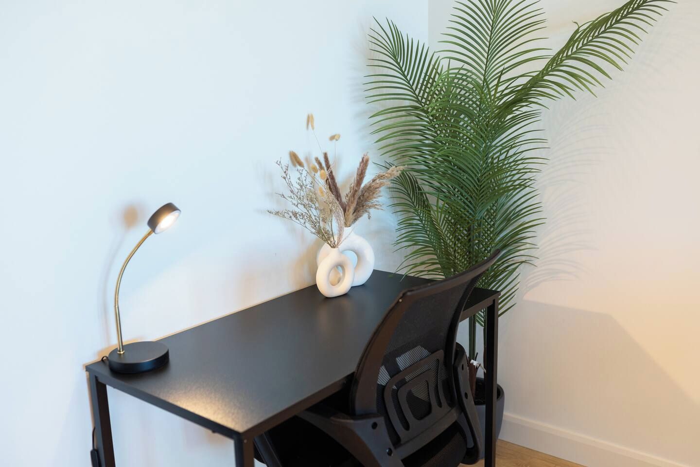 A desk with a lamp, a vase with dried plants, and a potted palm plant.