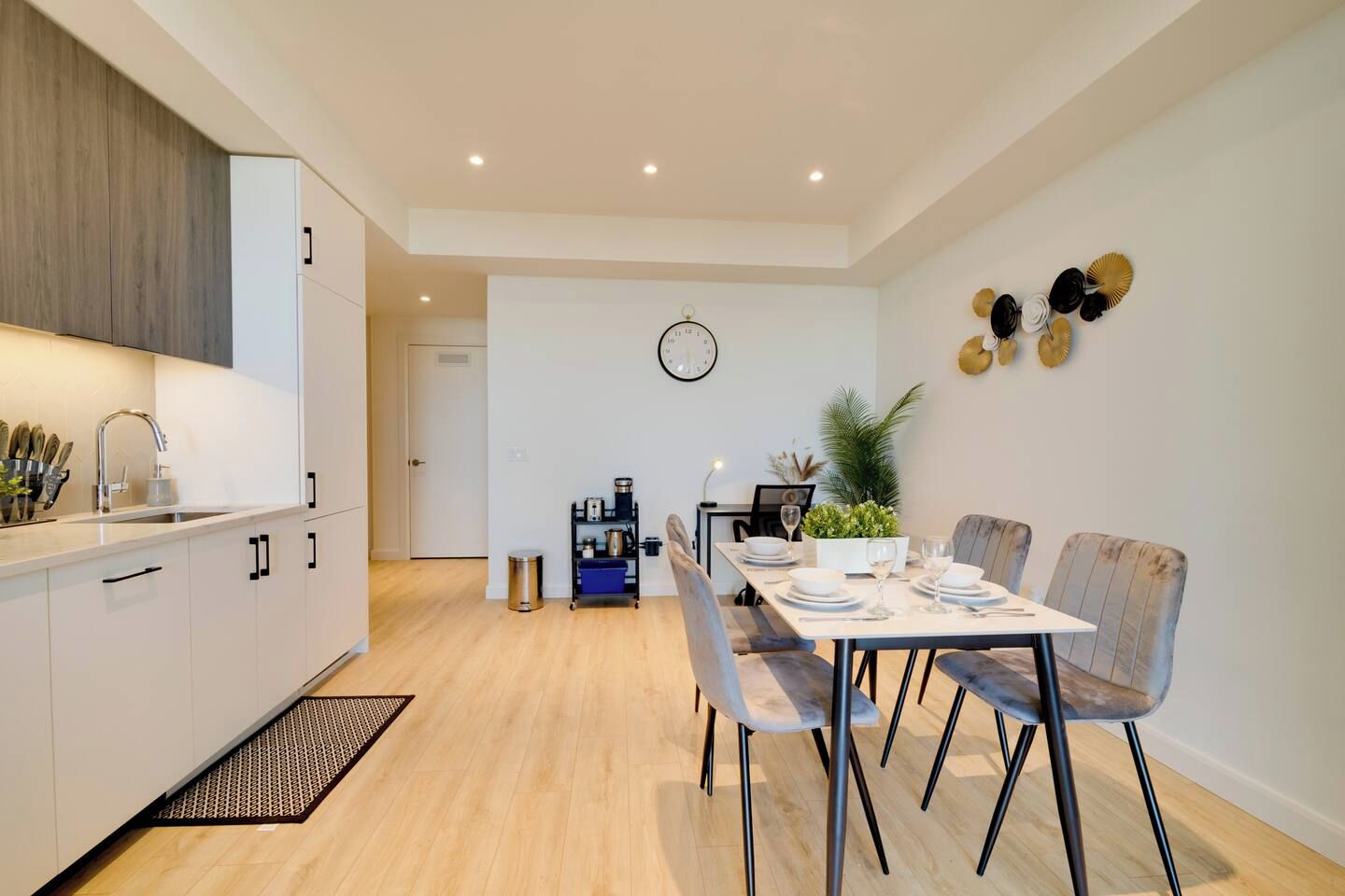 A modern kitchen with a dining area, featuring a built-in oven, a sink, and a coffee machine.
