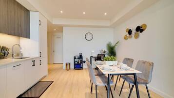 A modern kitchen with a dining area, featuring a built-in oven, a sink, and a coffee machine.