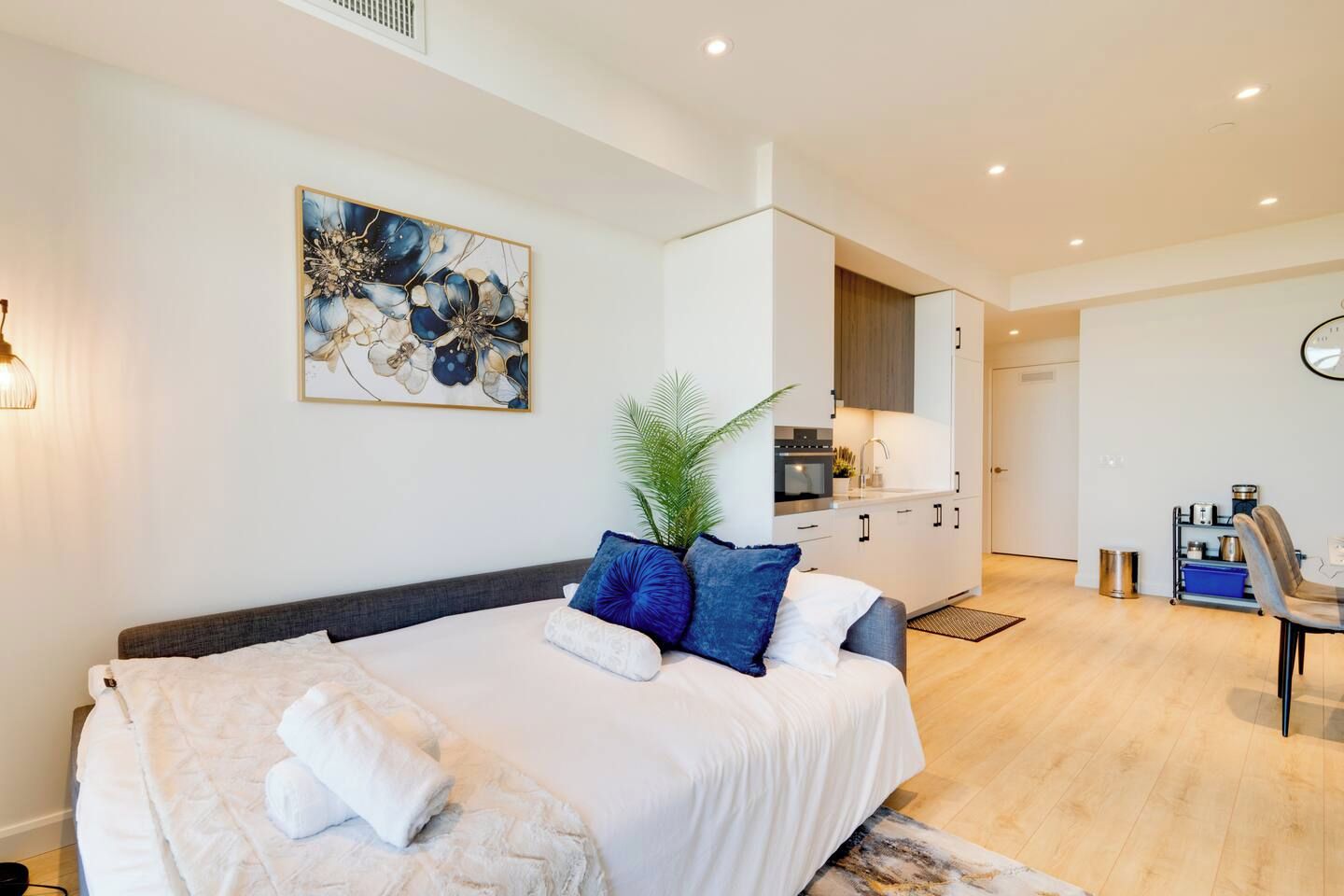 A modern bedroom with a large bed, a small kitchen area, and a dining table.