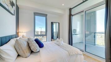 Un dormitorio moderno con una cama grande, vistas de la ciudad a través de una ventana y un balcón con puerta de cristal.